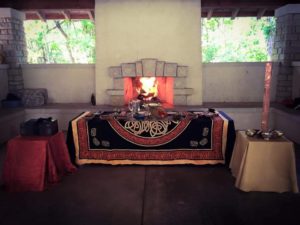 A altar covered in an orange and black tapestry sits before a merry fire